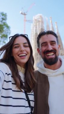 Kafkasyalı genç bir turist Barcelona 'daki Sagrada Familia' nın önünde dikey video görüşmesi yapıyor. Gülümseyen karı koca şehrin sokaklarında balayı tatilinin tadını çıkarıyorlar mutlu ve gülümseyen insanlar