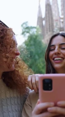 Dikey. Barcelona 'da Sagrada Familia' nın önünde cep telefonu kullanan tek genç bayan arkadaş. Avrupa şehrindeki güzel beyaz kızlar mutlu bir gülümsemeyle tatilin tadını çıkarıyorlar. Eğlence turizmi insanları