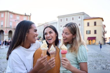 Üç genç kadın dondurma külahlarının keyfini çıkarıyorlar. Avrupa 'nın canlı şehir merkezinde yaz tatili maceraları boyunca gülüyorlar ve keyifli anları paylaşıyorlar.