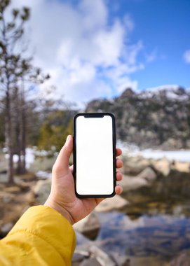 Dikey. Dağ manzarasında boş bir ekranla akıllı telefonu tutmak.