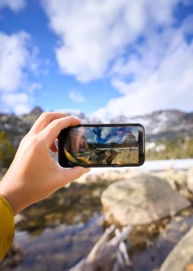 Dikey. Dağ manzarasında boş ekranlı bir akıllı telefonu tutan. Kafkasyalı adamın cep telefonuyla fotoğraf çekerken yakın plan