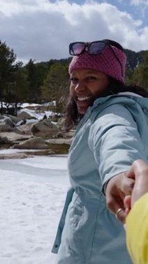 Dikey bakış açısı. Mutlu turist el ele tutuşuyor ve güzel donmuş dağ gölünü aşıyor. Kış tatillerinin tadını çıkarıyor.