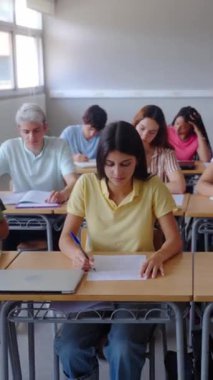 Dikey. Sınıfta birlikte çalışan bir grup çok ırklı öğrencinin ön görüntüsü. Sahne odaklanma, işbirliği ve akademik ortamda genç öğrencilerin çeşitliliğini vurguluyor