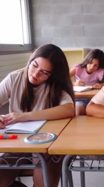 Dikey. Sınıfta birlikte çalışan bir grup çok ırklı öğrencinin ön görüntüsü. Sahne odaklanma, işbirliği ve akademik ortamda genç öğrencilerin çeşitliliğini vurguluyor