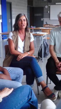 Dikey. Yanlarında beyaz erkek öğretmen var ve konuşuyorlar. Bir grup lise öğrencisi bir daire içinde oturmuş ders sırasında etkileşime geçiyorlar. Eğitim konsepti. Yüksek kalite fotoğraf