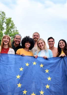 Dikey. Avrupa Birliği bayrağını gururla taşıyan çok ırklı arkadaş grubu birlik ve çeşitliliği sembolize ediyor. Açık havada neşeli bir atmosfer, birlikteliği ve kültürel uyumu teşvik ediyor. 