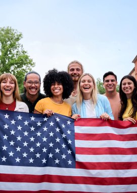 Dikey. Amerikan bayrağını gururla taşıyan çok ırklı bir grup arkadaş dışarıda Bağımsızlık Günü 'nü kutluyorlar. Parlak bir yaz ortamında birlik ve vatanseverlik duygusu ile neşeli bir atmosfer.