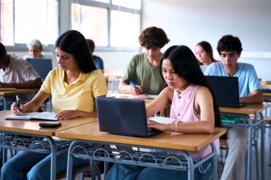 Cheerful Smiling Asian high school student girl using a laptop computer at class. A group of happy classmates in classroom. Education and technology. High quality photo