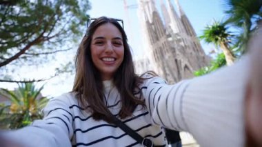 Genç beyaz kadınlar Barcelona 'da Sagrada Familia' nın önünde selfie çekiyorlar. Avrupa 'nın caddesinde gülümseyen güzel kız tatilin tadını çıkarıyor ve gülümsüyor. Komik turizm insanları.