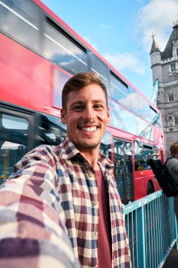 Dikey. Londra 'da selfie çeken genç bir adam kırmızı çift katlı bir otobüsle oradan geçiyor ve arka planda kule köprüsü var. İngiltere' nin başkentine yaptığı yolculuğun tadını çıkarıyor.