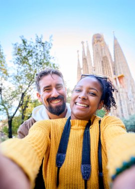 Dikey. Barcelona 'da Sagrada Familia' nın önünde selfie çeken genç bir çift. Şehrin sokaklarında gülümseyen karı koca tatilin tadını çıkarıyor ve gülümsüyor. Komik turizm insanları.