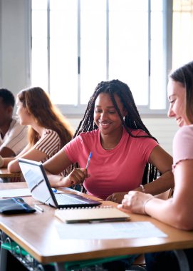 Dikey. Öğrenciler sınıfta bilgisayar laptopuyla çalışıyorlar. Gençler birlikte vakit geçiriyorlar. Genç beyaz ve neşeli Afrikalı Amerikalı kız birlikte çalışıyorlar. Yüksek kalite fotoğraf