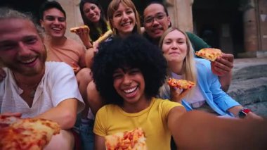 Turistik şehirde pizza yiyen bir grup gencin komik selfie 'si. İtalyan arkadaşlar dışarıda yemek yiyor, sokak ortamında gülüyorlar. Canlı şehir geçmişi ve neşeli bir ruh hali.