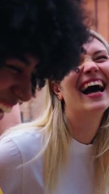 Dikey. Bir grup üniversite öğrencisi dışarıda birlikte yürüyor ve gülüyor, canlı bir öğrenci atmosferinde sınıflar arasında neşeli ve rahat bir anı paylaşıyorlar.