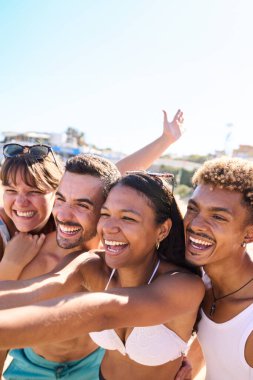 Mayo giymiş Z jenerasyonunun dikey fotoğrafları mutlu bir şekilde sahilde selfie çekiyorlar, neşeli ve kocaman gülücükler saçıyorlar. Çeşitli gençler yaz tatili maceralarının tadını çıkarıyorlar.