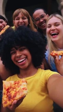 Dikey. Turistik şehirde pizza yiyen bir grup gencin komik selfie 'si. İtalyan arkadaşlar dışarıda yemek yiyor, sokak ortamında gülüyorlar. Şehir geçmişi ve neşeli ruh hali