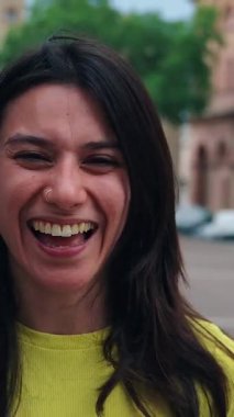 Etrafa gülümseyen bir kadının dikey portresi. Güzel kız mutlu ve sevimli ve pozitif bir ifadeyle poz veriyor. Çekici ve kendine güvenen beyaz kadın dışarıda eğleniyor.