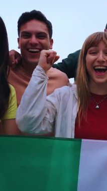 Dikey. İtalyan bayrağını gururla tutan çok ırklı bir arkadaş grubu vatanseverliği ve sporu, futbolu kutluyorlar. Neşeli bir atmosfer, birlik, coşku ve kültürel gurur.