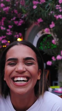 Dikey. Üç neşeli bayan arkadaş birlikte tatillerinin tadını çıkarıyorlar. Pembe çiçeklerle süslenmiş güzel bir sokakta kameraya bakıp neşeli ifadeler takınıyorlar.