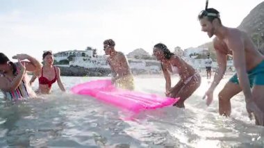 Mayolu bir grup mutlu ve neşeli genç arkadaş sahilde birbirlerine su sıçratarak su oyunu oynuyorlar. Nesiller boyunca insanlar tatilde iyi vakit geçiriyor.