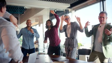 Hevesli iş ekibi başarıyı kutluyor, ofiste birlikte dans ediyor, bir amaca ulaştıktan sonra bir anlık sevinç ve arkadaşlığın tadını çıkarıyor.