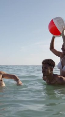 Dikey. Bikinili mutlu insanlar gün batımında denize koşup şişme topla oynuyorlar. Neşeli bayan arkadaşlar gölette su sıçratarak eğleniyorlar. Genç kadınlar yüzmeye gider, gölde yıkanırlar. Yavaş çekim