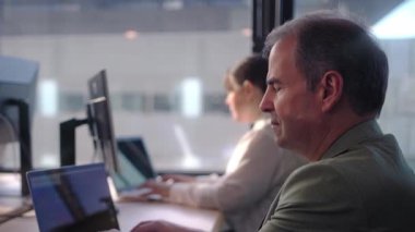 Profesyonel iş adamı dizüstü bilgisayara derinden konsantre olurken, bayan meslektaşı arka planda çalışıyor, odaklanmış işyeri işbirliği ve stratejik sorun çözme gösterileri yapıyor