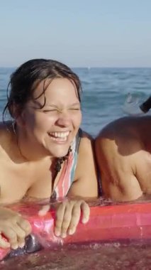 Dikey. Grup gülüşü ve çeşitli neşeli arkadaşlar deniz kıyısında şişme yatakta mayo giyerek yatıyorlar. Çok ırklı, heyecanlı genel dostlar güneşli tatillerin ve kumsalda boş vakitlerin tadını çıkarıyorlar.