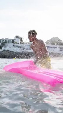 Mayolu mutlu ve neşeli genç arkadaşlardan oluşan dikey bir grup sahilde birbirlerine su sıçratarak su oyunu oynuyorlar. Nesiller boyunca insanlar tatilde iyi vakit geçiriyor.