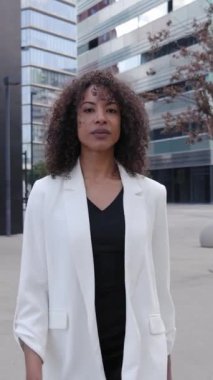 Dikey. Güçlenmiş Afrikalı iş kadını ofisten kendinden emin çıkıyor ve farklı iş arkadaşlarına benziyor. Zarif genç yetişkin başarılı resmi bayan girişimci şehir finans merkezinin dışında geziniyor.