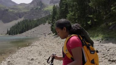 Siyah kadın bir dağ gölünün kenarına yaklaşıyor ve Moraine Gölü 'nü veya Yosemite Milli Parkı' nı andıran barışçıl doğayla çevrili manzaraya hayran olmak için duruyor.
