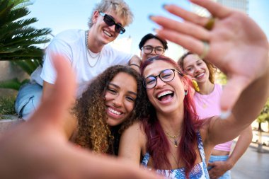 Neşeli genç öğrencilerden oluşan bir grup ellerle bir çerçeve oluşturuyor, güneşli bir günde birlikte gülüyor ve eğleniyorlar, anılarını yakalıyorlar ve birlikte vakit geçiriyorlar.