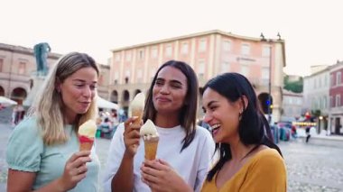 Üç tane çok ırklı genç kadın güneşli bir İtalyan köy meydanında dondurma külahlarının keyfini çıkarırken gülümseyip sohbet ederken büyüleyici bir Akdeniz ortamında rahatça oturuyorlar.