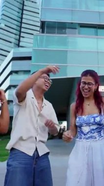 Dikey. Canlı bir grup genç çok kültürlü arkadaş şehrin ortasında neşeli bir şekilde dans ediyor, güneşli bir günde hayatı kutluyor ve birbirlerine eşlik ediyorlar.