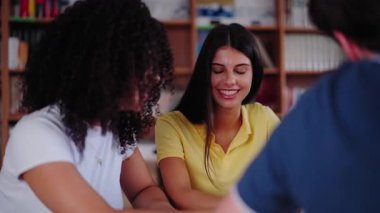 Genç lise öğrencilerinin iki çok kültürlü kızı sınıfta birlikte çalışıp gülümsüyor ve kütüphanede oturuyorlar. Mutlu Nesiller z sınıf arkadaşları beyin fırtınası yapıyor çalışıyor ve eğleniyor.