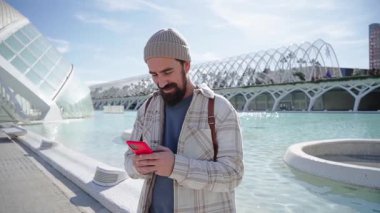 Valencia 'daki bilim parkında cep telefonu kullanan yakışıklı beyaz adam. Neşeli genç turist güneşli kış gününde cep telefonuyla konuşurken mutlu duruyor. Bir erkek çağrıya cevap veriyor. Kültür Turizmi.