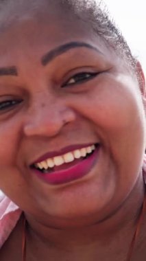 Afrikalı bir kadının dikey portresi artı boyut deniz kenarında güvenle gülümseyen, vücut pozitifliğini, çeşitliliği, doğal güzelliği ve neşeli yaşam tarzını temsil eden.