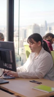 Dikey. Parlak, modern bir ofiste çalışan kadın, şehir görüşüne sahip, verileri analiz ederken ve ortak bir çalışma alanında görevleri tartışırken odaklanma ve işbirliğini birleştiren.