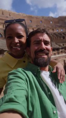 Dikey. Gülümseyen ırklar arası bir çift Roma 'daki Colosseum' da tatilin tadını çıkarıyor, geziler sırasında neşeli bir selfie çekiyor ve tarihi mimariyi keşfediyorlar..