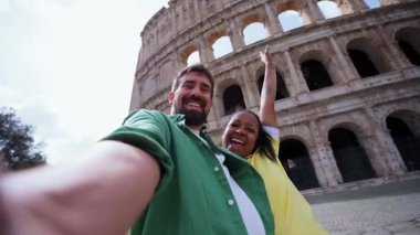 Roma, İtalya 'daki kolezyumu ziyaret eden mutlu, etnik çeşitlilikte turistlerin güneşli gökyüzü altında gülümseyerek ve unutulmaz maceralarının tadını çıkarırken çekilmiş selfie videosu.