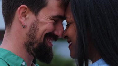 Alınları birbirine değmiş, gözleri kapalı, gülümseyen, şefkat, güven ve derin bir bağ kuran ırklar arası bir çiftin yakın çekimi..