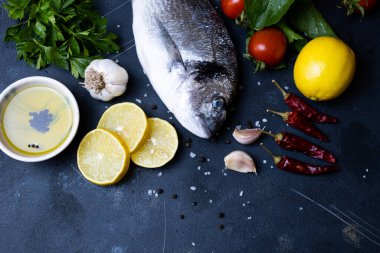 Çiğ çipura ya da dorada deniz balığı pişirmeye hazır. Limon manzaralı, arka planda sarımsak. Akdeniz mutfağı, deniz ürünleri, sağlıklı beslenme..