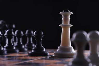 Yakın plan. Siyah piyon beyaz vezirin karşısında duruyor. Karanlık bir arka planda satranç taşlarıyla çevrili