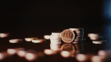 İki metal sikke kulesi ve etraflarına saçılmış madeni paralar. Yukarıdan, paralar yavaş çekimde vernikli bir masaya ve bozuk para kulelerine düşer. Yumuşak odak