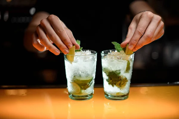 男性バーテンダーの手がきれいに緑のミントの葉でバーカウンターに冷たいモヒートカクテルでメガネを飾る — ストック写真