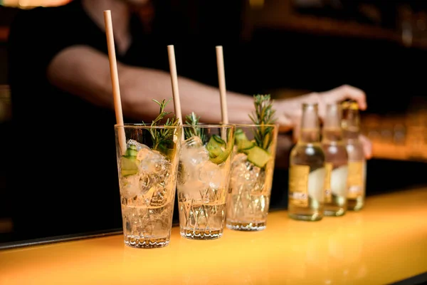 Selective focus on glasses with cold gin tonic cocktail with drinking straws and bottles on bar counter