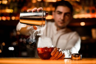 Süzgeçli çelik bardak ve barmenin elinde soğuk içecekle yakın plan. Döküm kokteylinin süreci