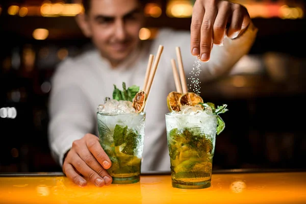 stock image Beautiful close-up view on transparent glass with cold mojito cocktail and hand of man bartender pouring sugar on it