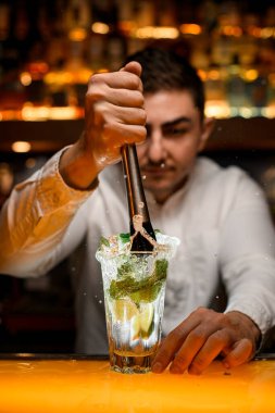 Erkek barmenin eli, şeffaf bardakta mojito malzemelerini ustalıkla sıkıyor.