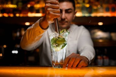 Şeffaf camların yakın plan mojito kokteyli. Erkek barmenin eli camda mojito malzemelerini karıştırır ve sıkar.
